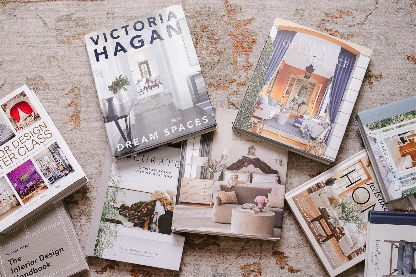 Interior design books arranged on a patterned rug, with an open design book and layered home inspiration titles.